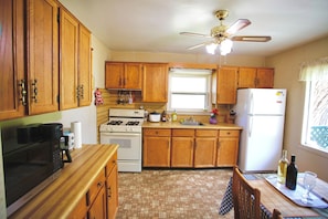 Kitchen features a microwave, stove, sink, and refrigerator, with a ceiling fan above the countertop.