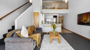 A modern living room with a grey sofa, a wooden coffee table, and a staircase leading to an upper level. - Alpine Three Bedroom Two Bath Apartment (Queenstown)