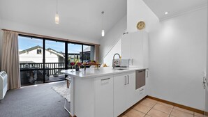 A modern kitchen with a large island, a built-in oven, and a sink. There is a window providing a view of the outside. - Alpine Three Bedroom Two Bath Apartment (Queenstown)