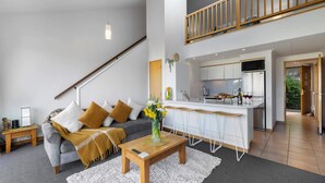 A modern apartment with a living room, kitchen, and a staircase leading to an upper level. - Alpine Three Bedroom Two Bath Apartment (Queenstown)