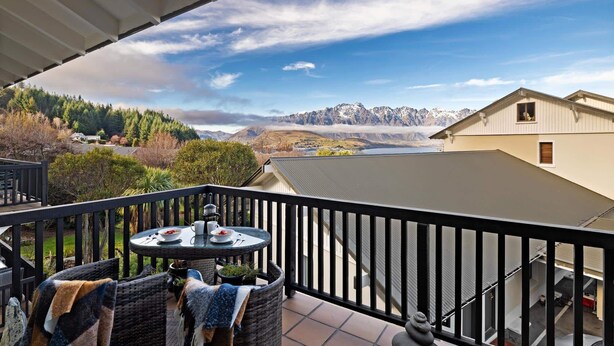 A balcony with a table and chairs, overlooking a mountainous landscape and a body of water. - Alpine Three Bedroom Two Bath Apartment (Queenstown)
