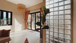 A spacious living area with a sofa, a large potted plant, and a sliding glass door leading to an outdoor area. - Xom House Bien Ho (Bien Ho)