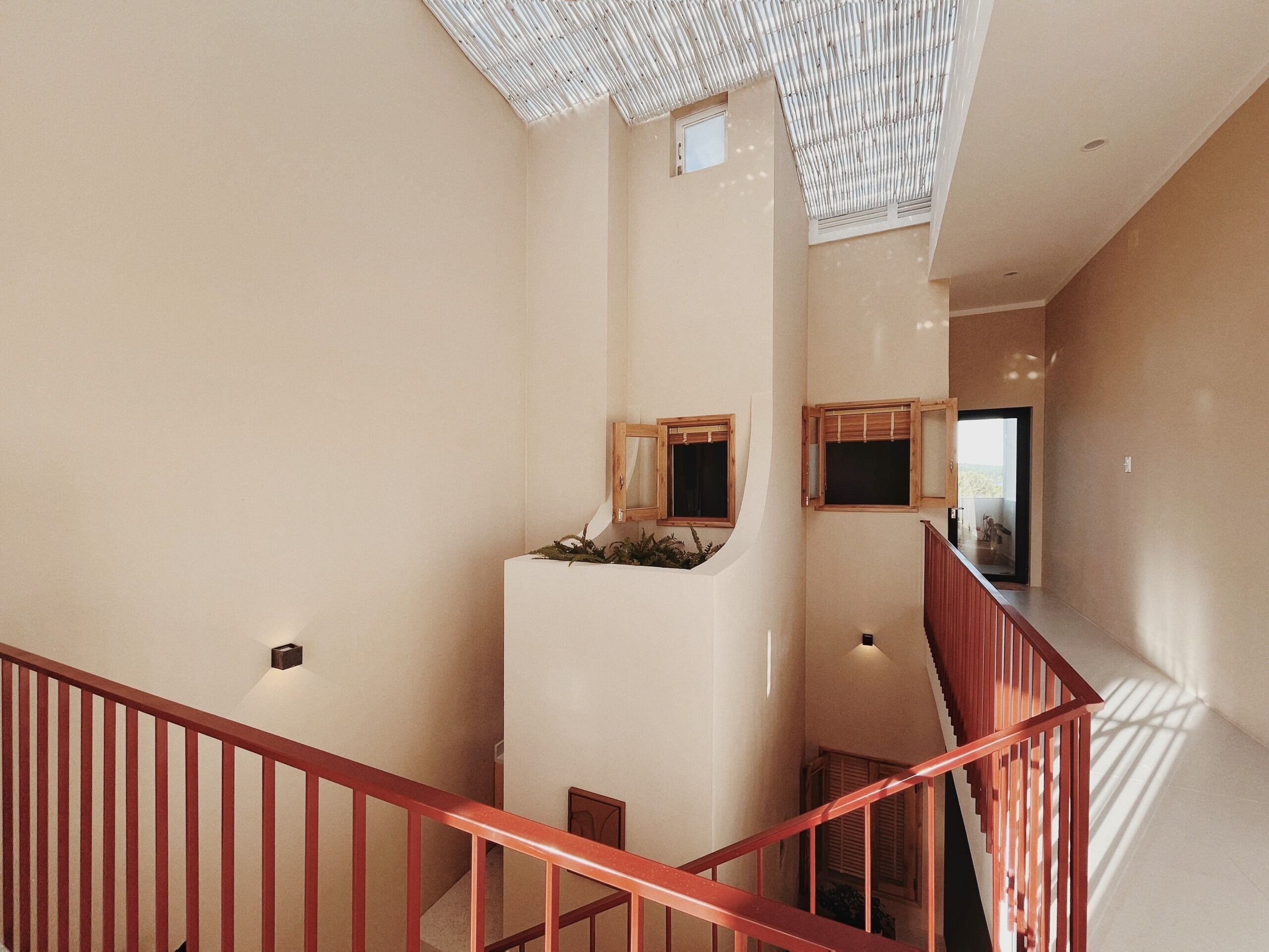 A multi-level interior with a staircase, wooden window frames, and a ceiling with a bamboo-like design.