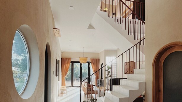 A spacious interior with a staircase leading to an upper level, large windows, and a view of the outdoors. - Xom House Bien Ho (Bien Ho)