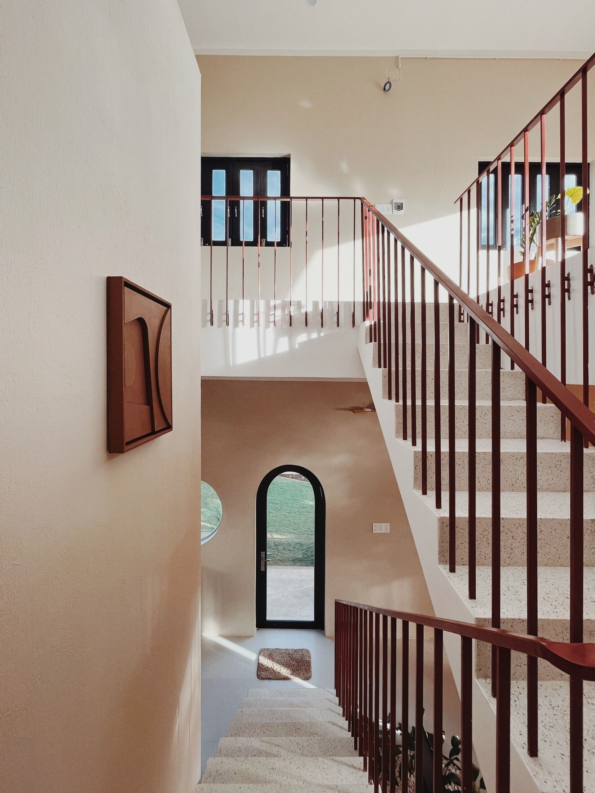 Eine Treppe mit Holzgeländer und Blick auf einen Garten durch einen Rundbogen.