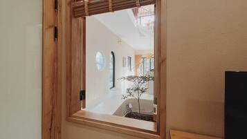 A wooden-framed window with a view of a hallway and a plant inside.