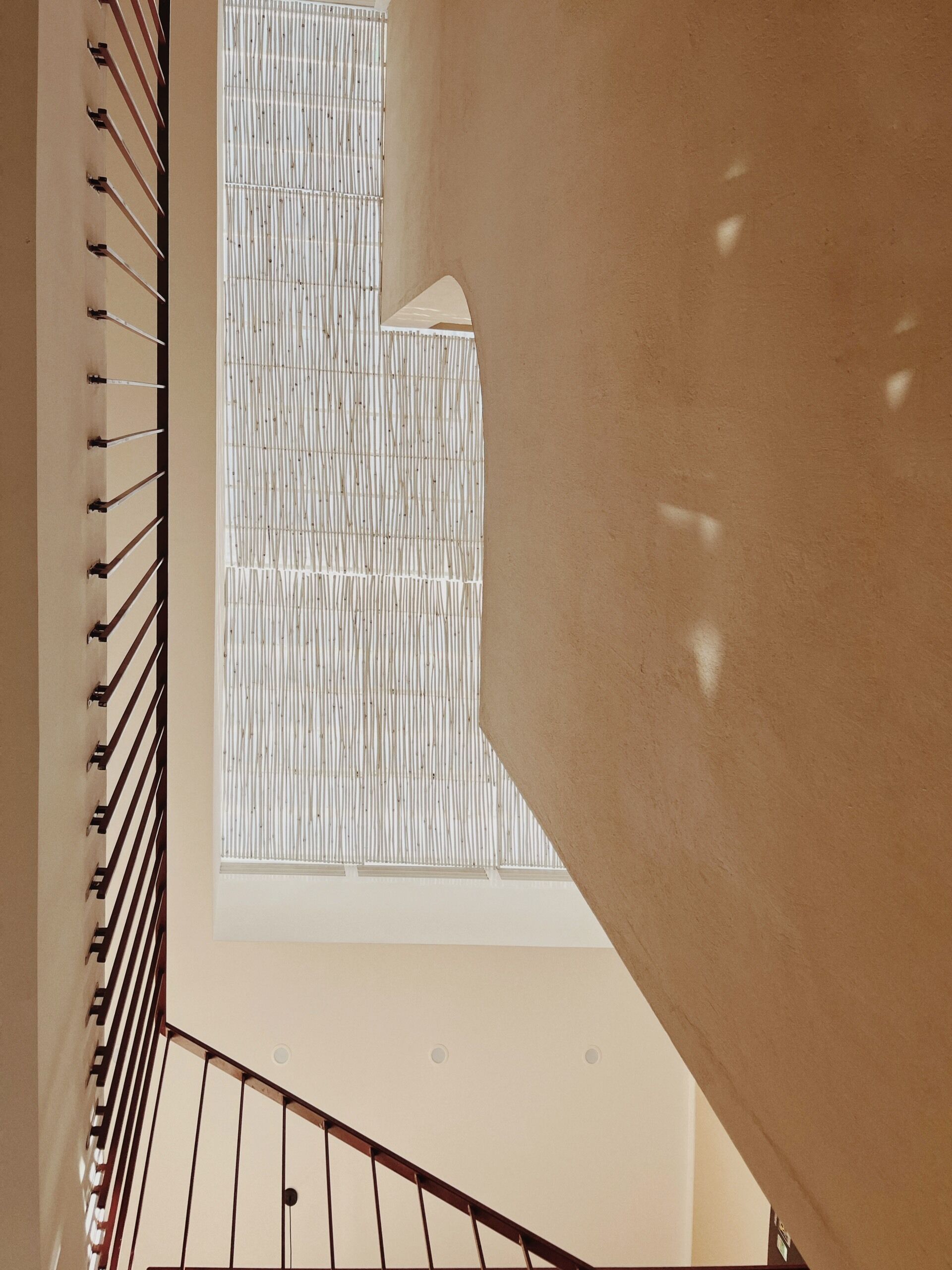 Una escalera con barandilla en espiral y vistas a una pared con textura y una ventana con persianas verticales.