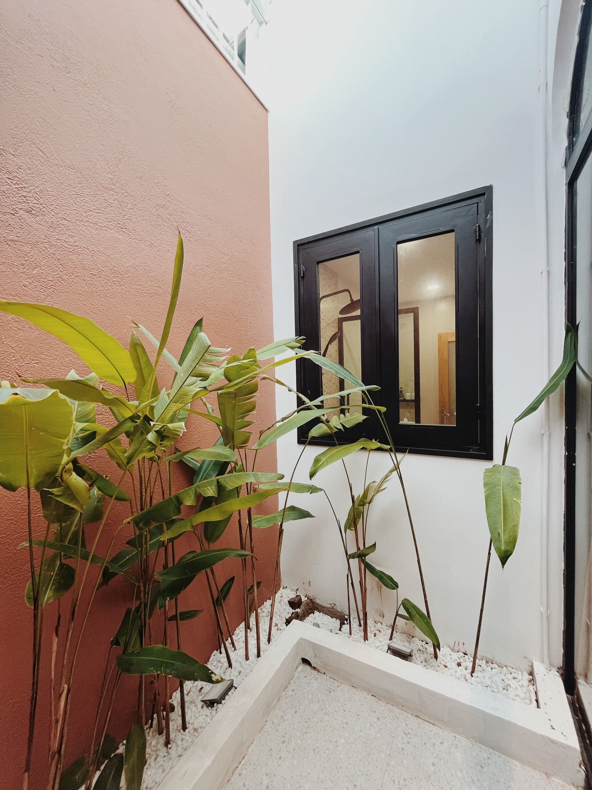 Un estrecho pasillo exterior con una pared blanca y otra rosa, que conduce a una puerta con marco negro y un pequeño ventanal encima.