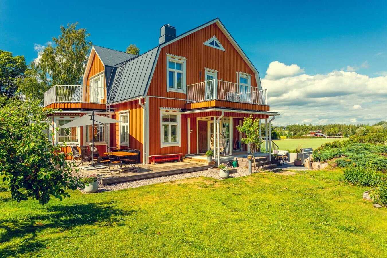 Ein großes, zweistöckiges Haus mit Balkon, überdachter Terrasse und gepflegtem Rasen.