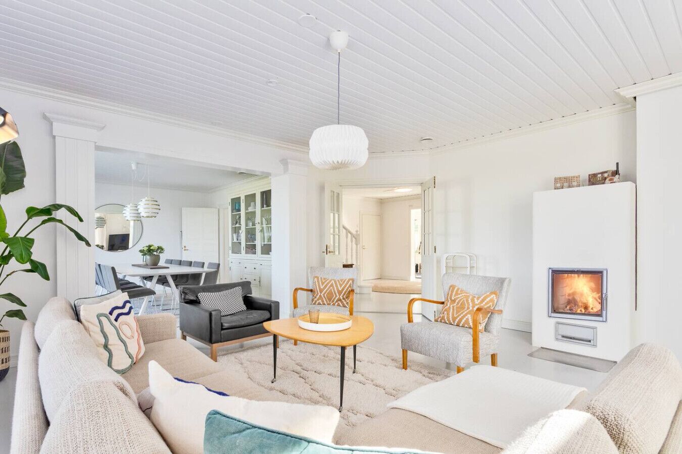 A modern living room with a fireplace, a dining area, and a kitchen visible through an open door.