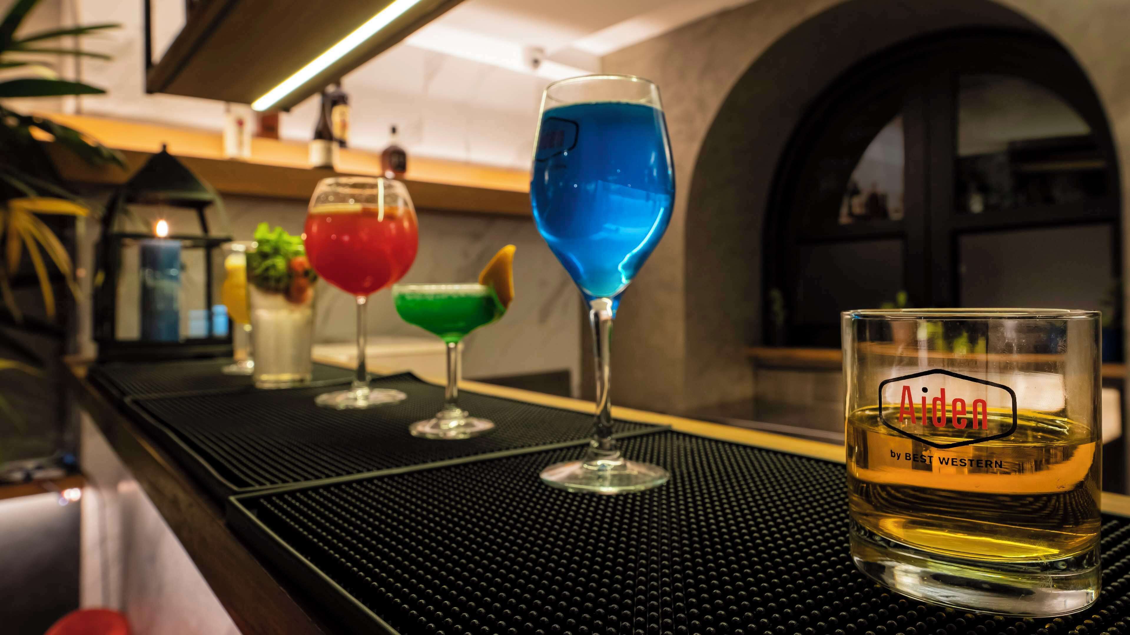 Zona de bar con diferentes vasos de cócteles y un vaso con la etiqueta "Aiden by Best Western".