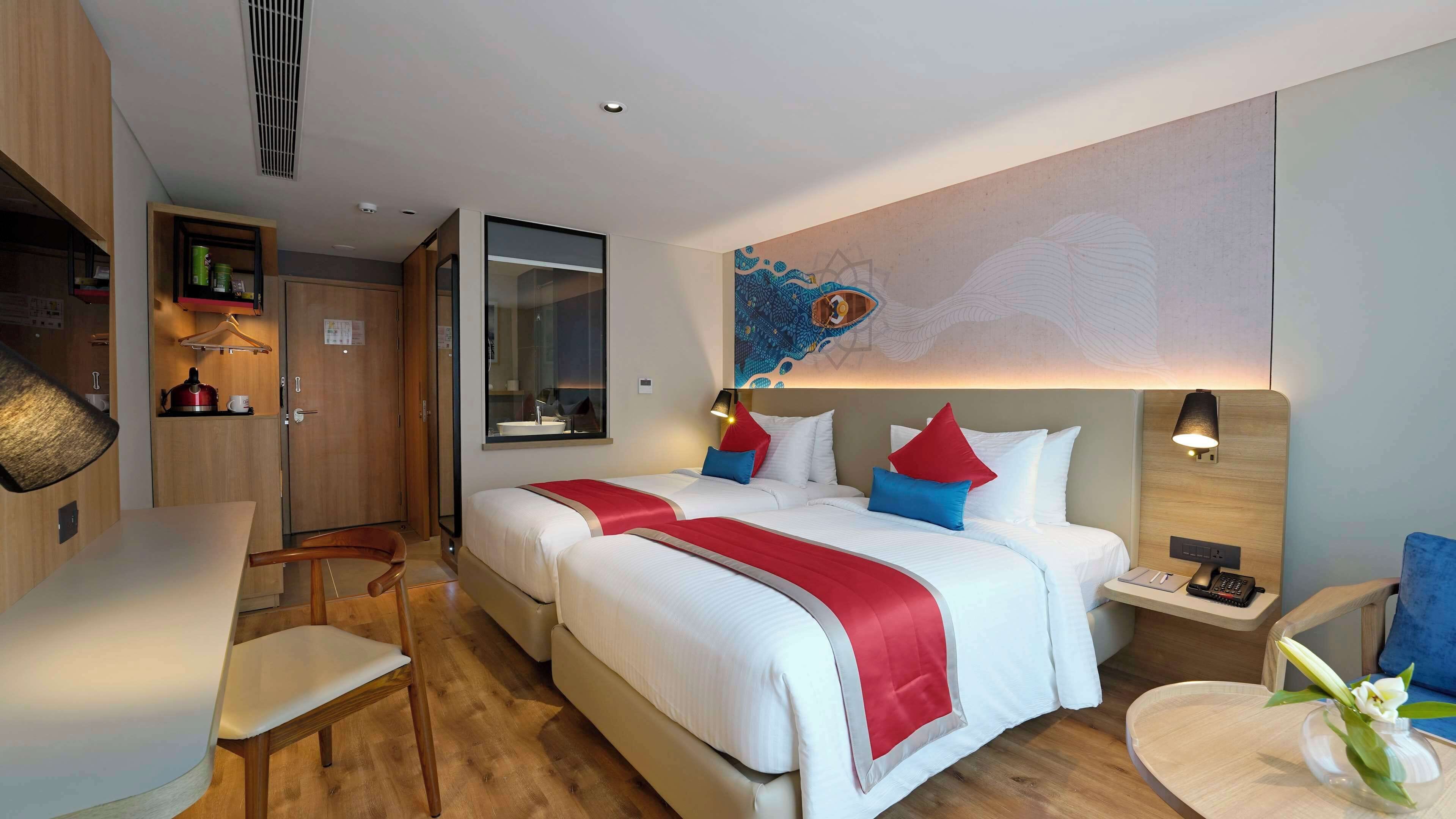 Une chambre d’hôtel avec un grand lit, un bureau, une chaise, une petite table avec un vase et une œuvre d’art accrochée au mur.