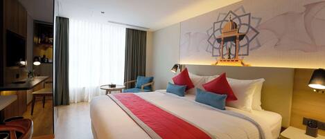 A hotel room with a large bed, a desk, a chair, a small table, and a wall with a geometric design.