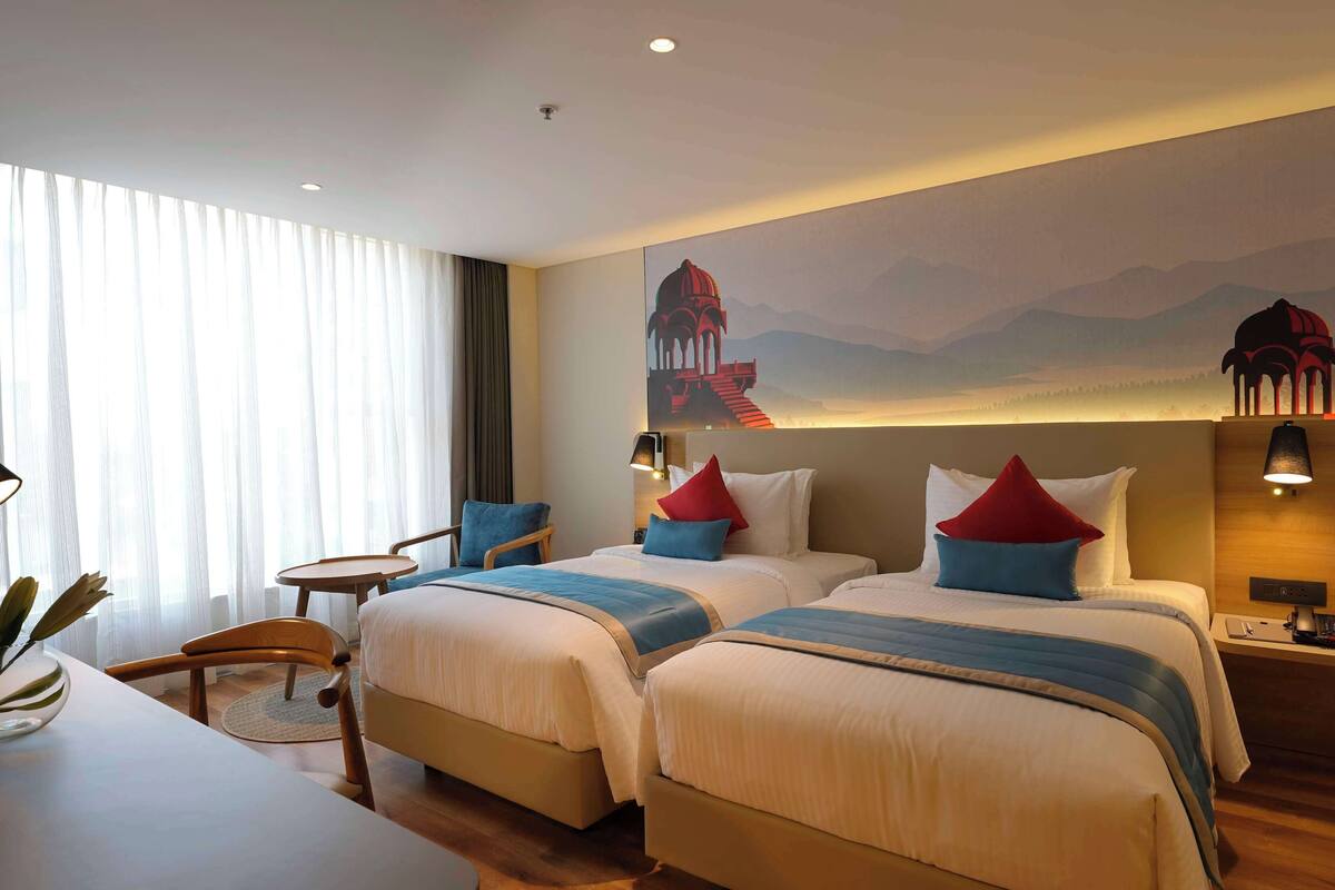 Une chambre d’hôtel avec deux lits, un bureau, une chaise et une grande fresque murale.
