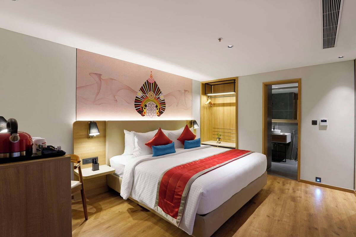 Une chambre d’hôtel moderne, dotée d’un grand lit, de tables de chevet, d’un bureau et d’une salle de bain visible à travers une porte ouverte.