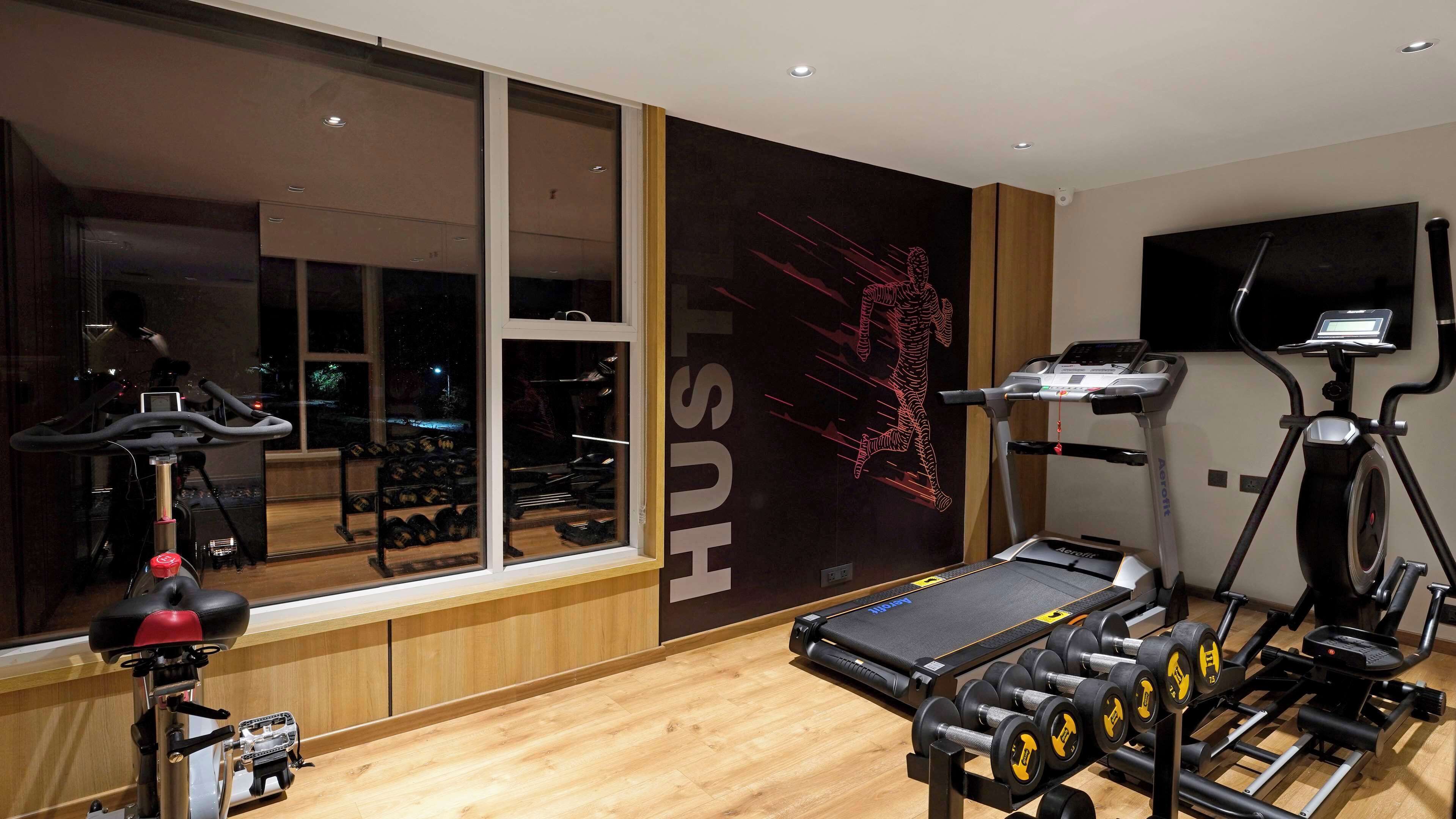 A modern gym with cardio equipment, weight benches, and dumbbells.