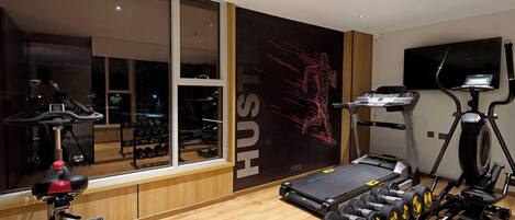 A modern gym with cardio equipment, weight benches, and dumbbells.