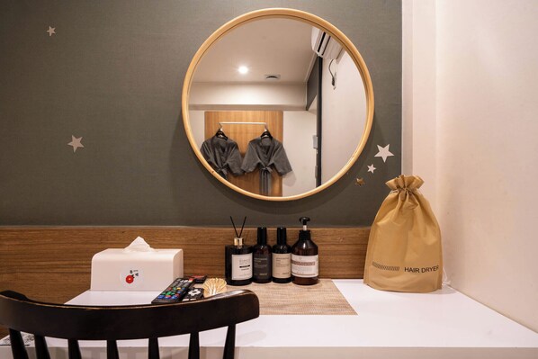 A bathroom with a round mirror, a towel rack with two towels, a hair dryer bag, and a tissue box.