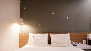 A hotel room with a bed, two pillows, a bedside table with a phone, and a wall with star decals. - Haeundae Dongbeck Hotel (Busan)