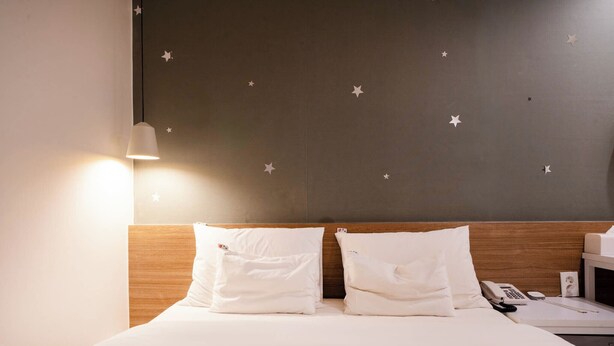 A hotel room with a bed, two pillows, a bedside table with a phone, and a wall with star decals. - Haeundae Dongbeck Hotel (Busan)