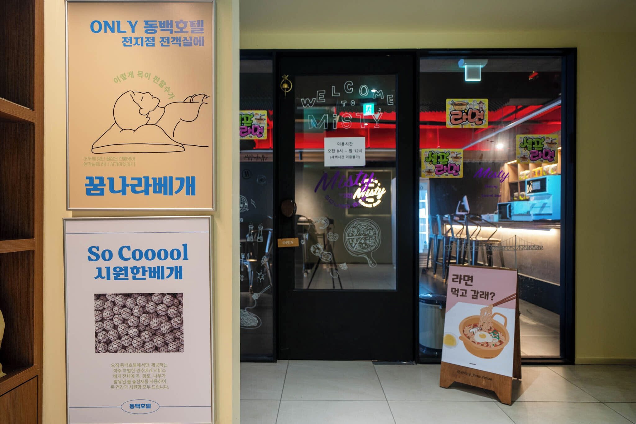 A restaurant entrance with a neon sign, a menu board, and a signboard with Korean text.