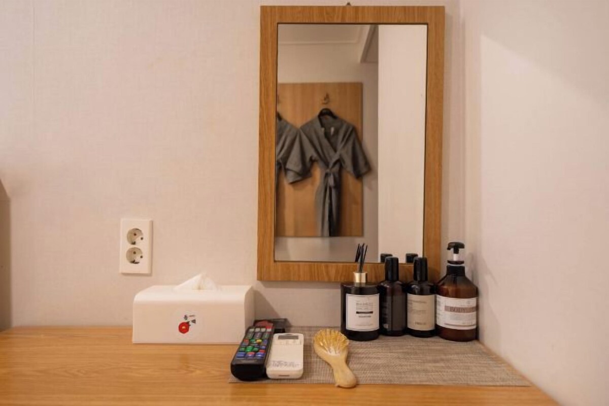 A hotel room with a wooden bedside table, a white tissue box, a remote control, a hairbrush, and toiletries.