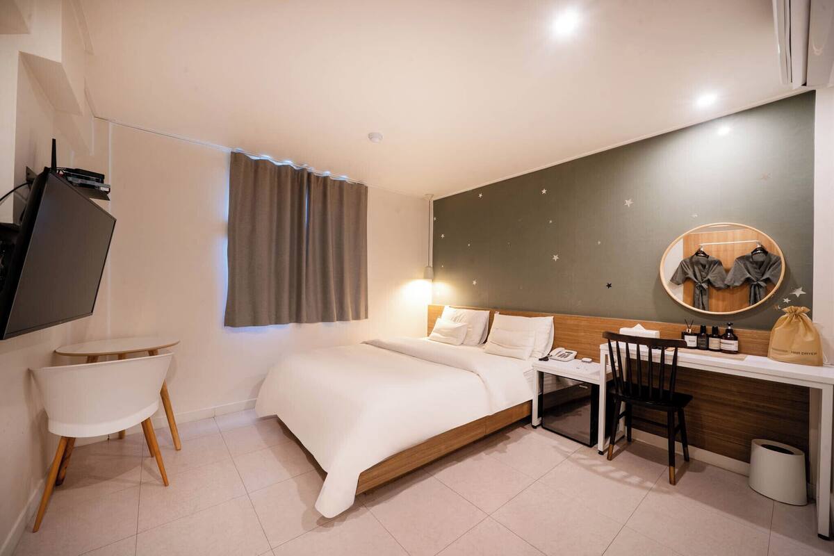 Una habitación de hotel moderna con una cama, un escritorio, una silla, un televisor y un espejo.