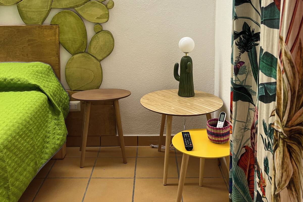 A room with a bed, a small round table, a cactus sculpture, a remote control, and a patterned curtain.