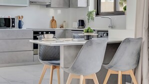 Une cuisine moderne avec des meubles de couleur grise, une cuisinière encastrée, un four à micro-ondes et un évier. On y trouve deux chaises grises et un petit îlot central sur lequel est posé un saladier rempli de fruits.