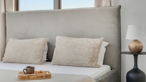 Un lit avec deux oreillers à texture, une table de chevet avec une lampe et un plateau avec une tasse et un panier.