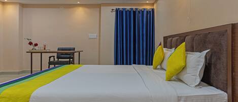 A hotel room with a large bed, a desk with a chair, a blue curtain, and a ceiling fan.