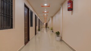 A long, well-lit hallway with a fire extinguisher on the wall, doors on one side, and potted plants along the other. - Itsy Hotels Kashi Grand, BHU (Varanasi)