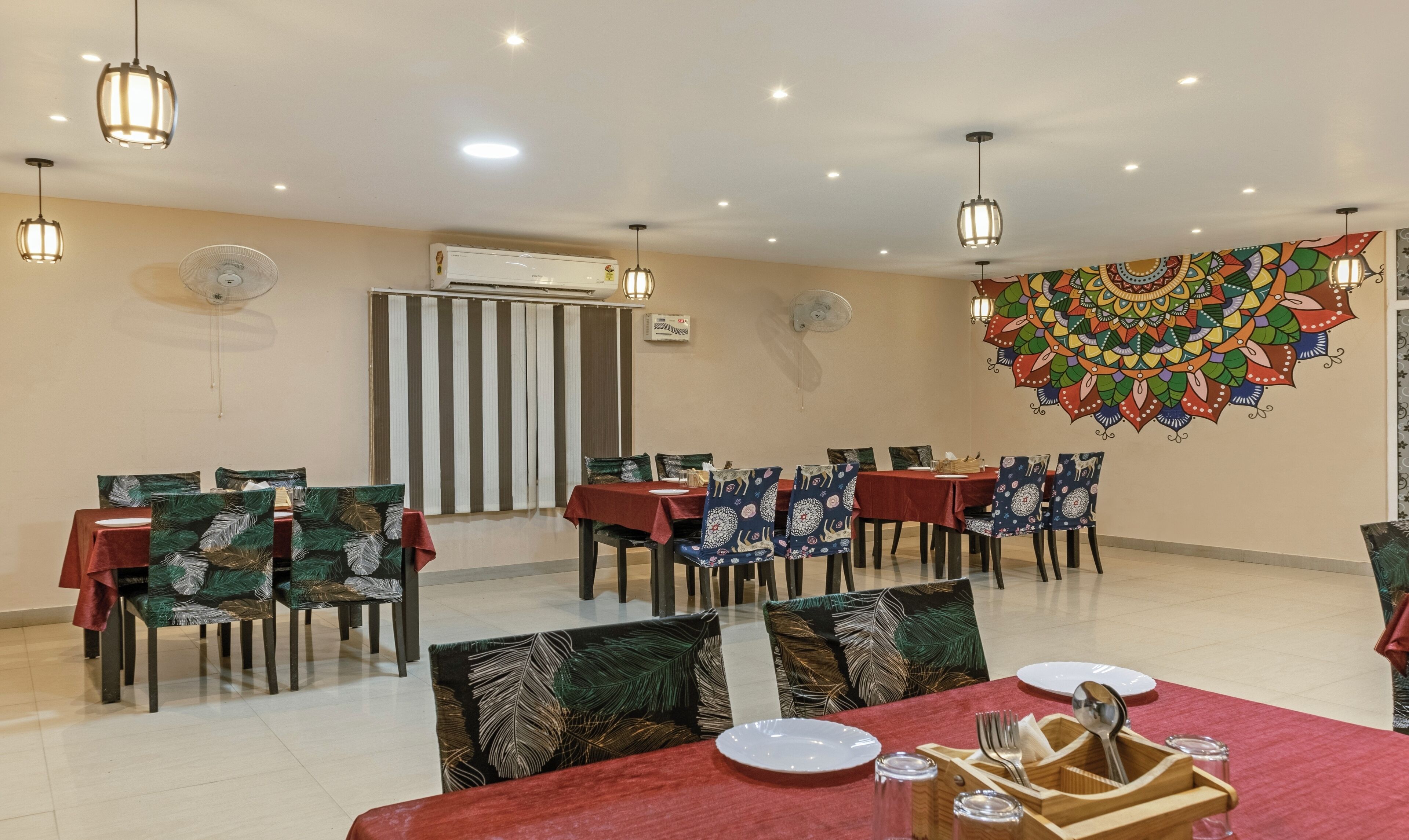 A dining area with tables set for four, chairs with patterned cushions, and a decorative wall mural.