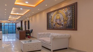 A modern lobby with a reception desk, a sofa, a coffee table, and a large decorative painting. - Itsy Hotels Kashi Grand, BHU (Varanasi)