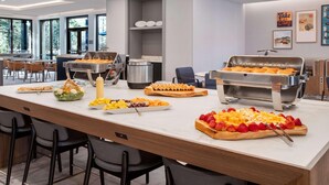 Ein reichhaltiges Buffet mit verschiedenen Speisen, einer Grillstation und einem Sitzbereich mit Stühlen.