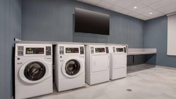 A laundry facility with four washing machines and a large flat-screen TV on the wall.