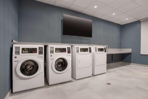 A laundry facility with four washing machines and a large flat-screen TV on the wall.