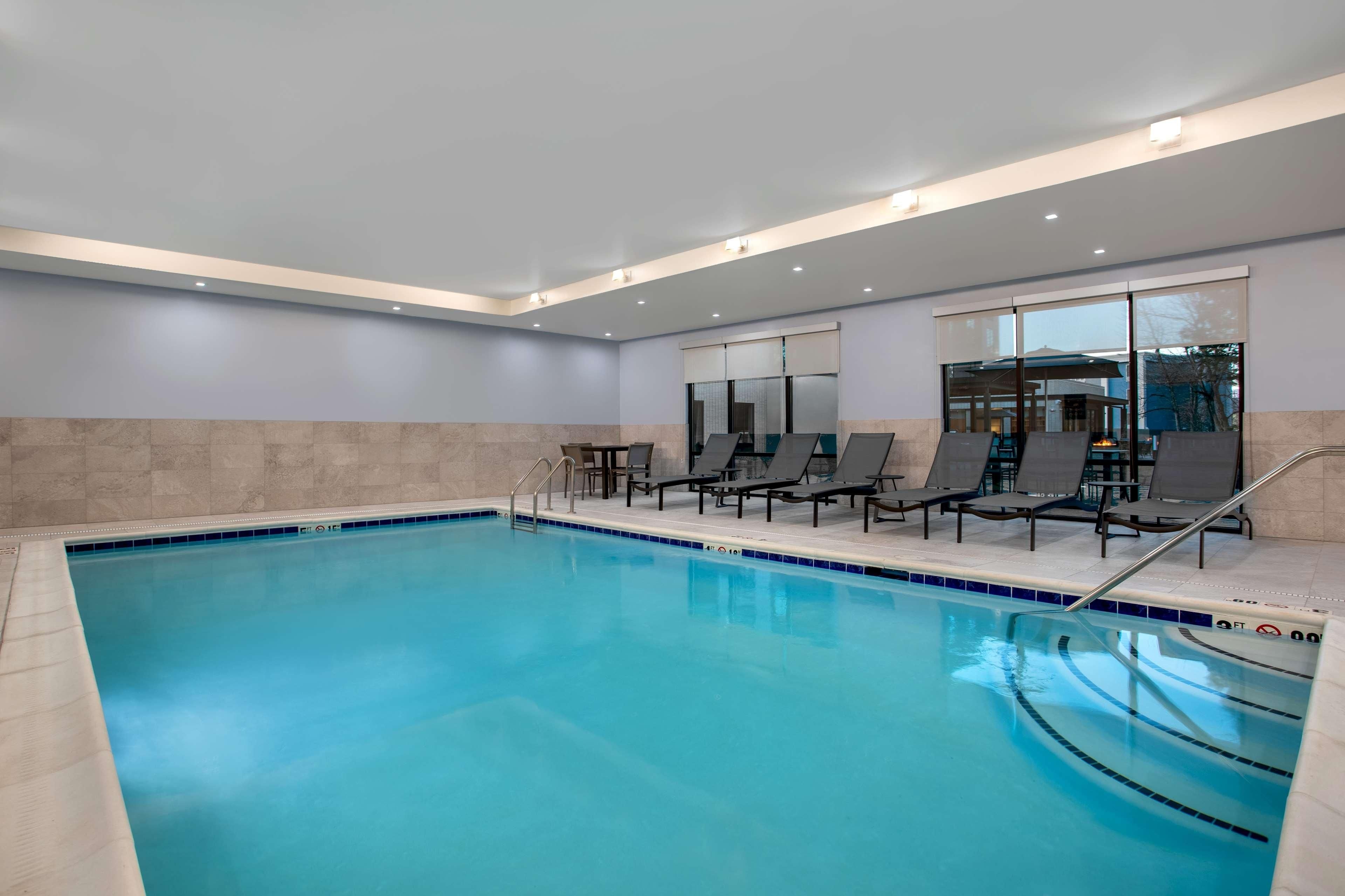 An indoor swimming pool with clear blue water, surrounded by lounge chairs and a tiled floor.