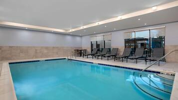 An indoor swimming pool with clear blue water, surrounded by lounge chairs and a tiled floor.