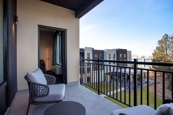 A balcony with a wicker chair and a table, a door leading to an interior room, and a view of modern buildings and a grassy area. - (Missoula)