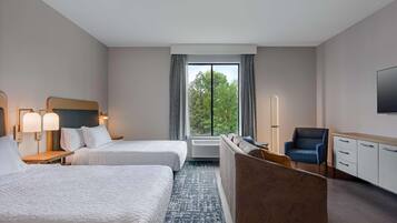 A hotel room with two beds, a sofa, a chair, a TV, and a window with a view of trees.