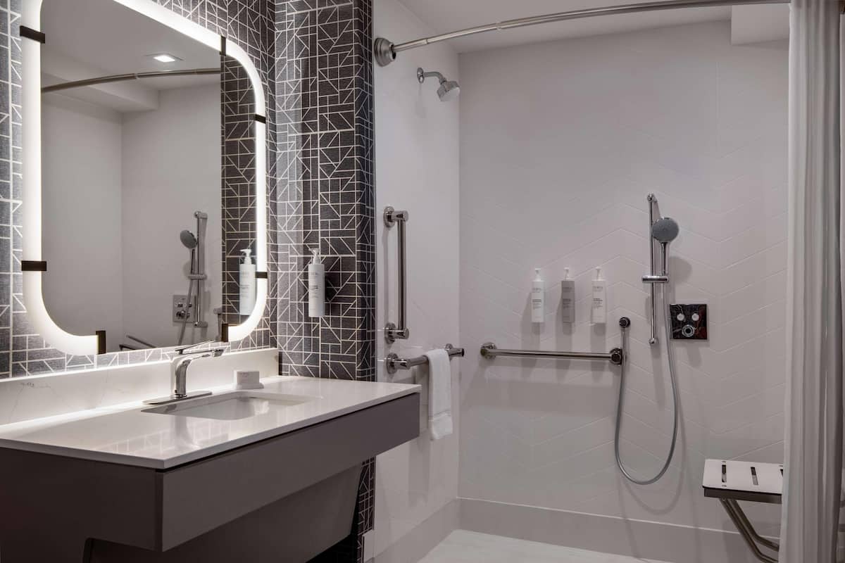 A modern bathroom with a white sink, a large mirror, and a shower area with a handheld showerhead.