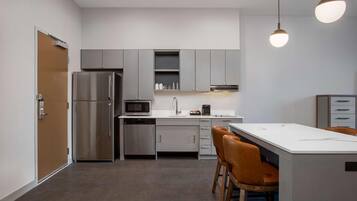 A modern kitchen with a refrigerator, microwave, coffee maker, and bar stools.