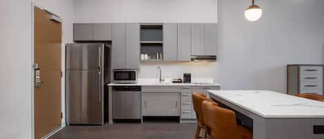 A modern kitchen with a refrigerator, microwave, coffee maker, and bar stools.