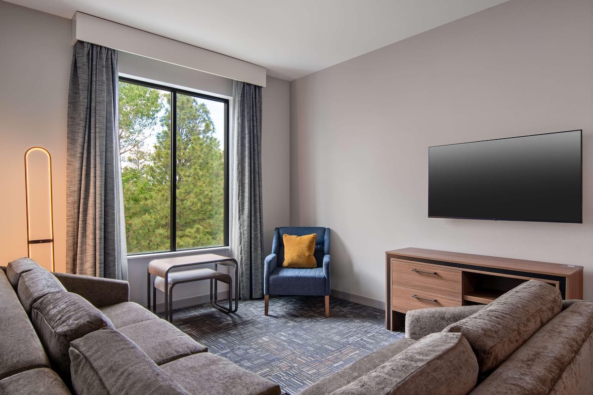 Una habitación de hotel moderna con un ventanal grande, un televisor de pantalla plana, un sofá, una silla y un escritorio.