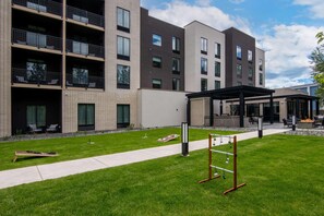 A multi-story building with balconies, a covered outdoor seating area, and a well-maintained lawn.