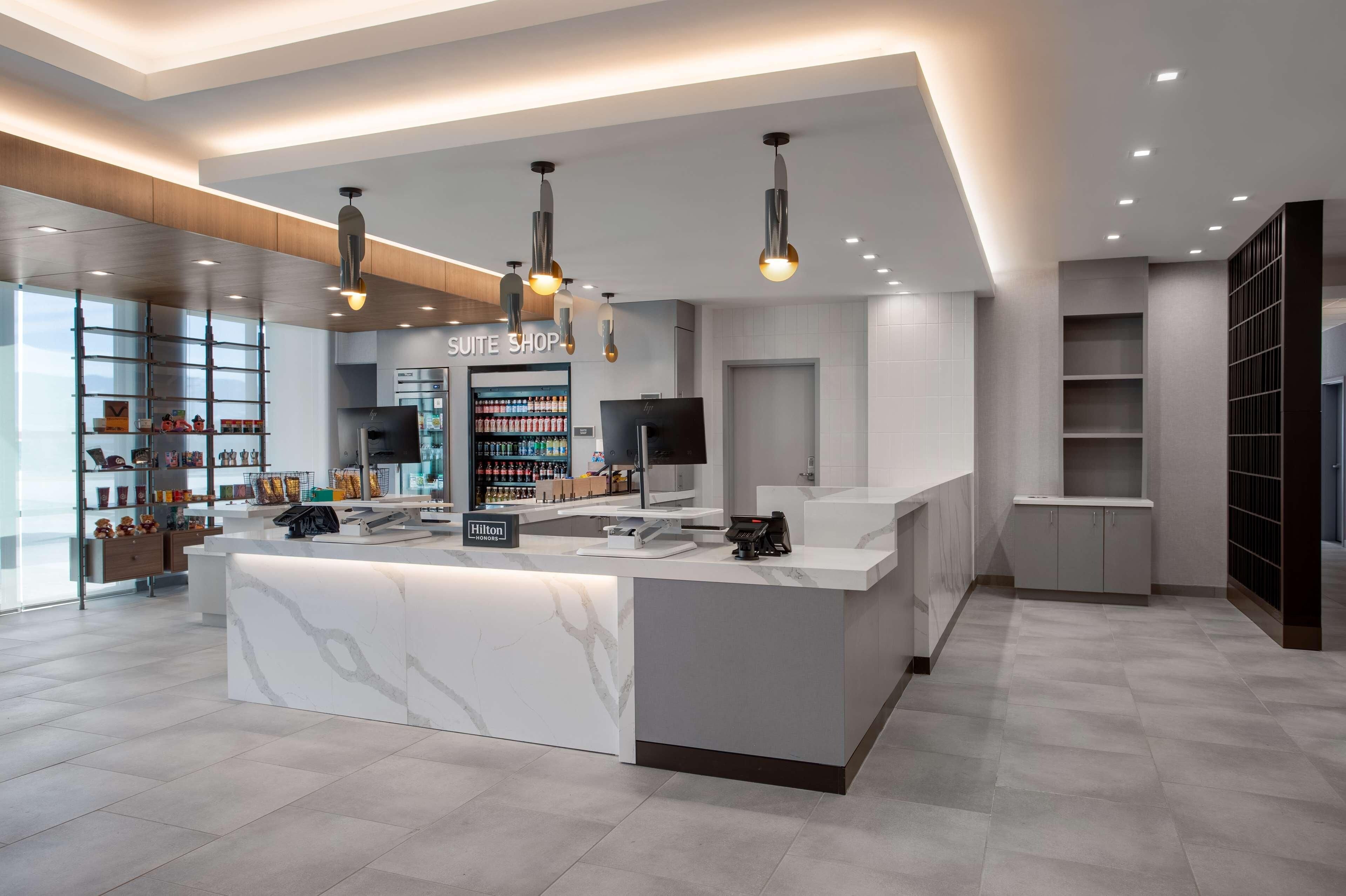 A modern hotel reception area with a marble counter, overhead lighting, and a visible minibar.