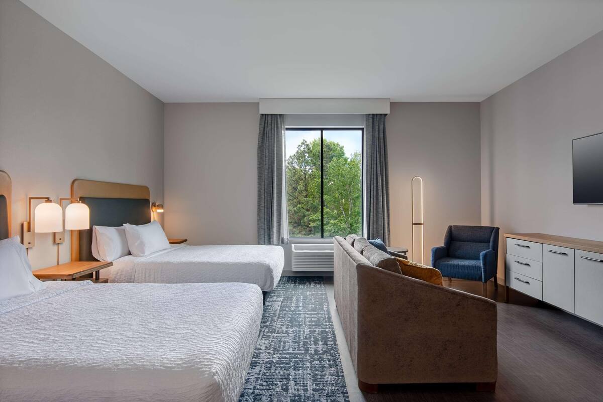 Habitación de hotel con dos camas, un sofá, una silla, un televisor y una ventana con vistas a árboles.