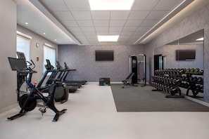 Une salle de sport équipée de tapis de course, d’un appareil elliptique, d’un banc de musculation et d’un porte-haltères.