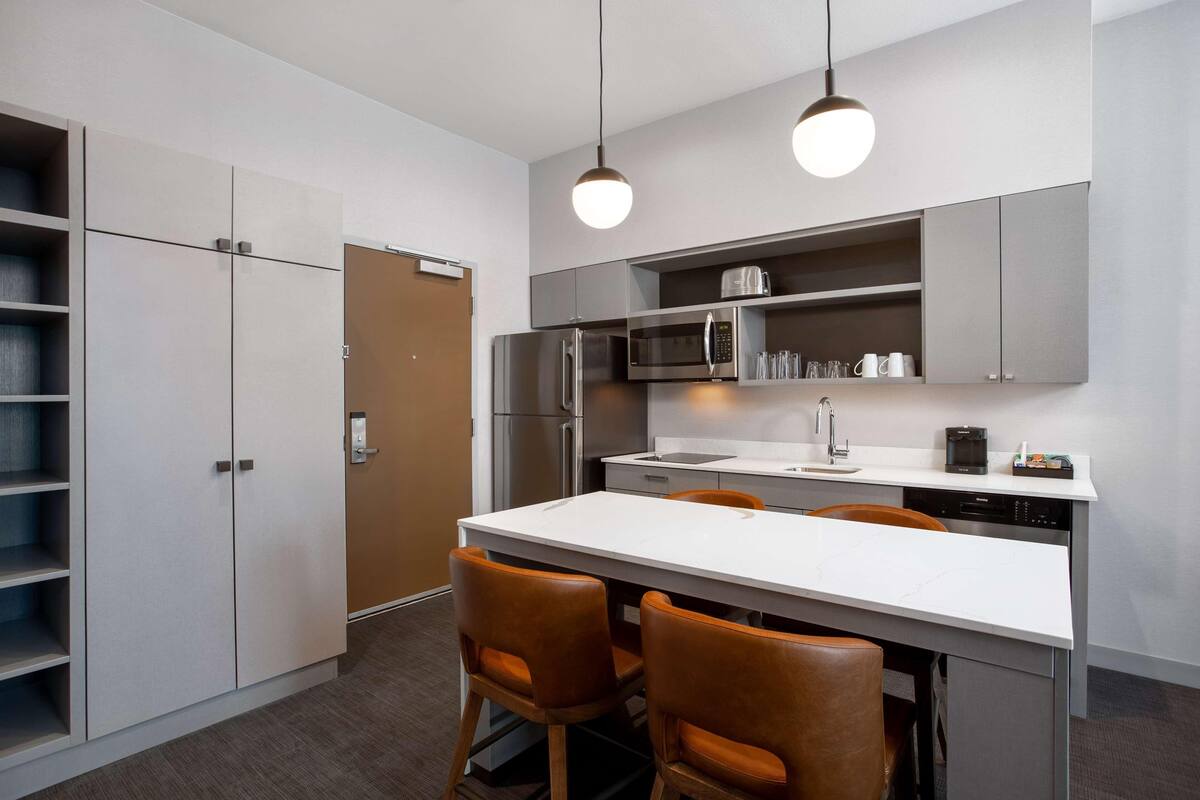 Una cocina moderna con una isla blanca, electrodomésticos de acero inoxidable y sillas de cuero marrón.
